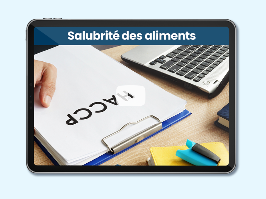 Table avec ordinateur et paquet de feuilles sur lequel est écrit HACCP. Texte sur l'image: Salubrité des aliments